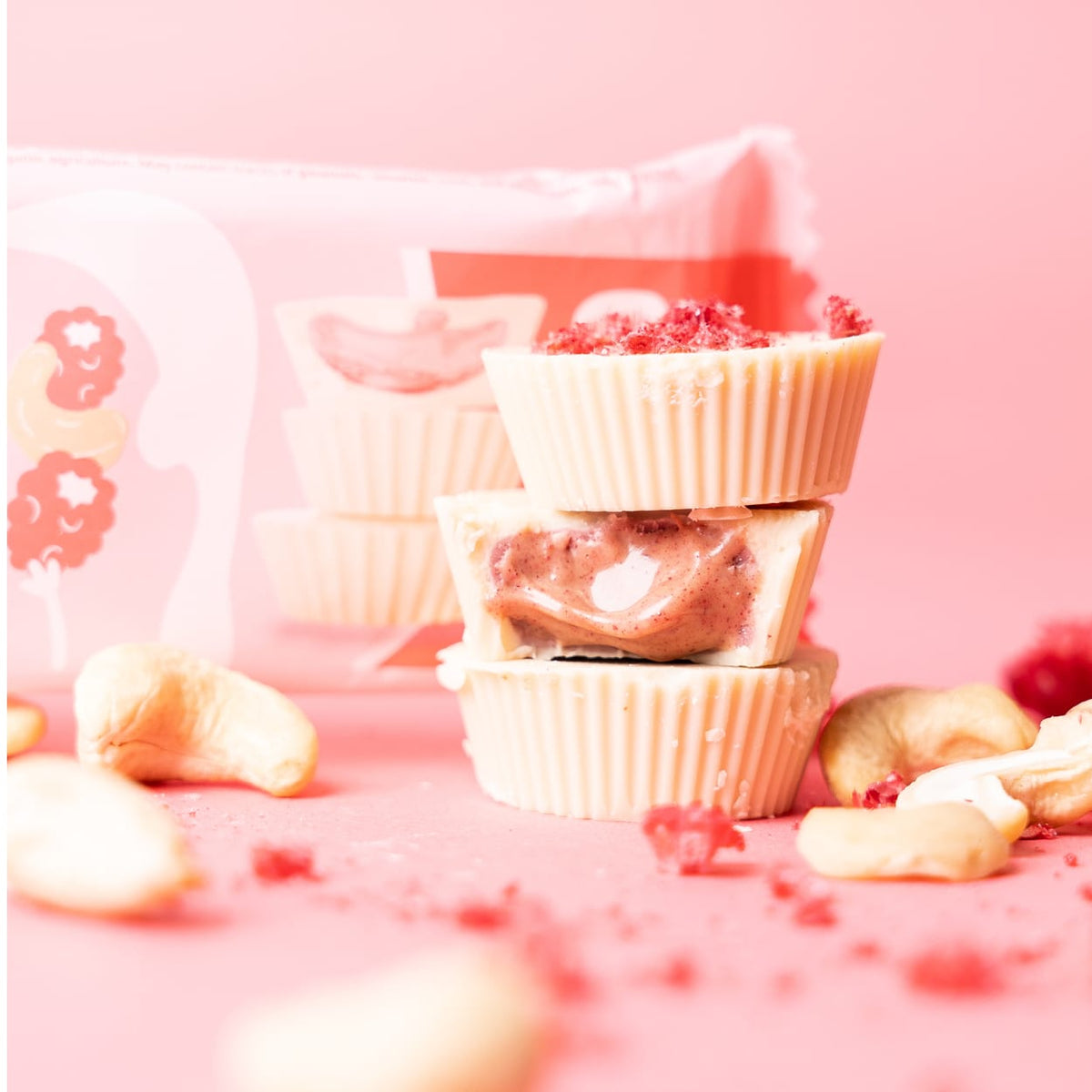 Bio Cashew Butter Cups Raspberry Rumble, gestapelt, einer halbiert, mit Cashewkernen und Himbeerstückchen