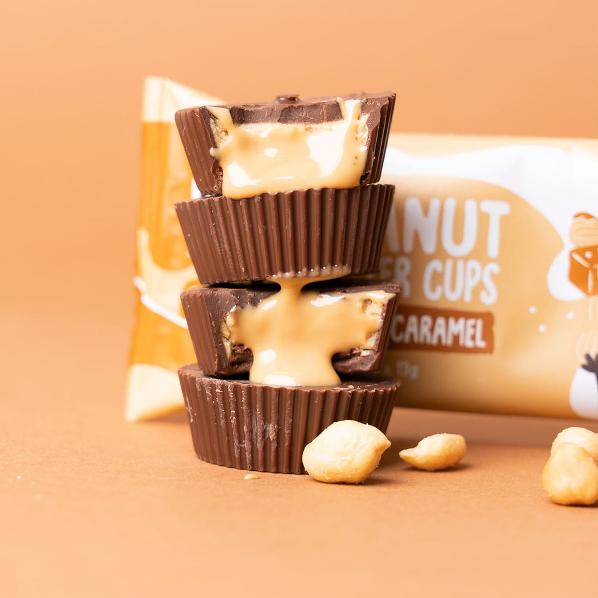 Drei gestapelte Bio Nutbutter Cups mit Karamellfüllung, die herausläuft, und Erdnüssen auf braunem Hintergrund