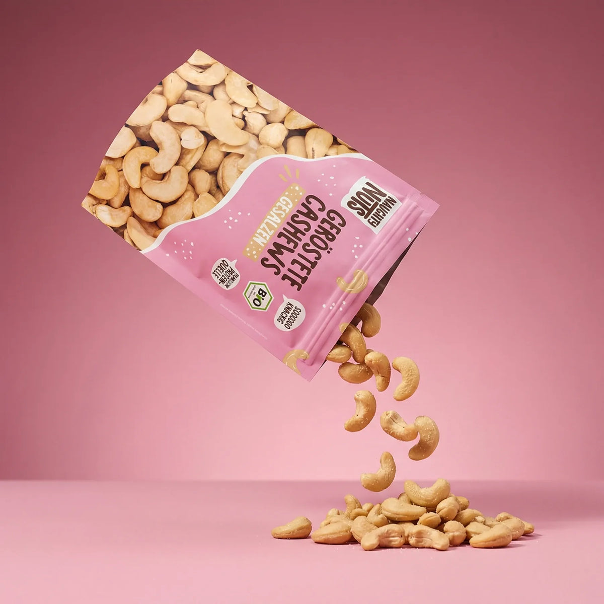 Geröstete Cashews gesalzen fallen aus einer rosa Verpackung auf einen rosa Hintergrund - AI-generated